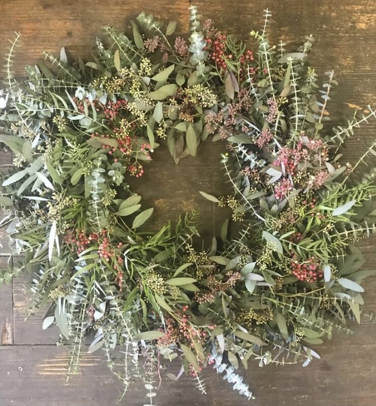 A loose wreath of silver eucalyptus and dried sprigs, laid on weathered wood