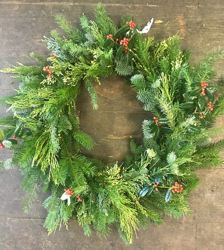 A full evergreen wreath of cedar and fir with small red berries, on wood