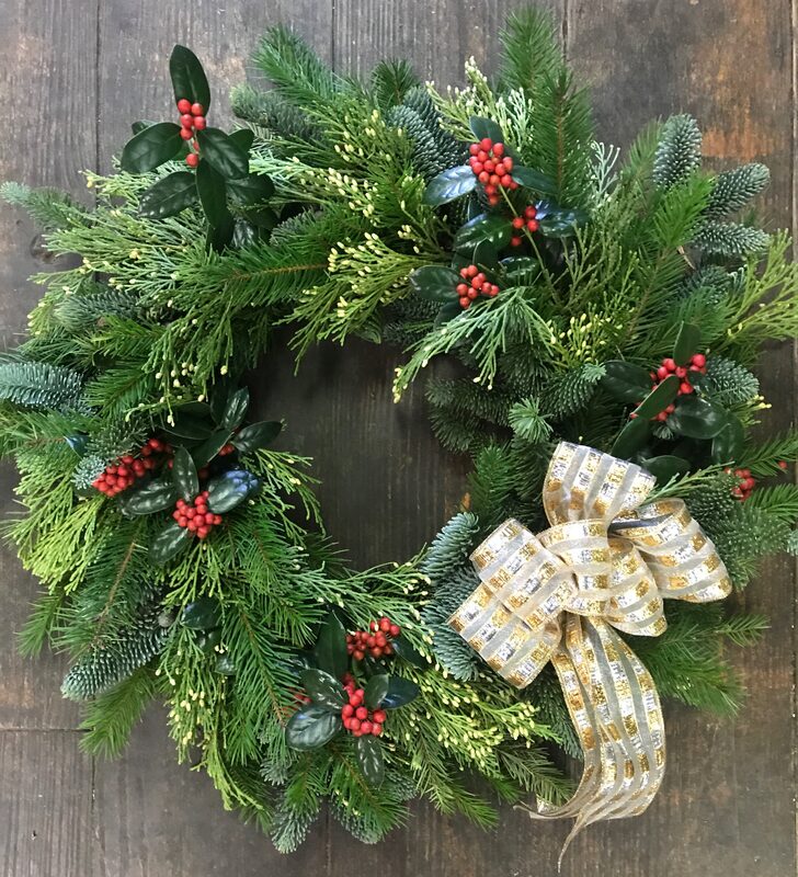 An evergreen wreath with holly berries and a gold-checked ribbon bow, on wood
